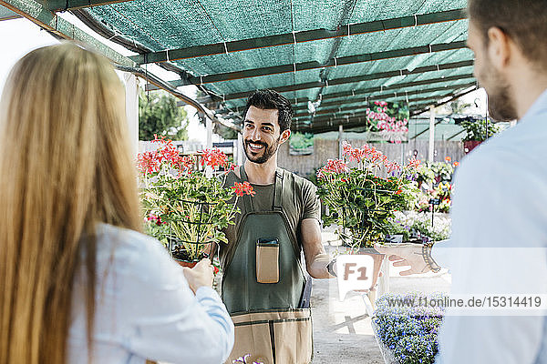 Glückliche Mitarbeiterin in einem Gartencenter  die Kunden Pflanzen zeigt