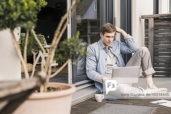 Mann sitzt auf der Terrasse und benutzt einen Laptop