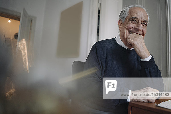 Porträt eines glücklichen älteren Mannes  der zu Hause am Tisch sitzt