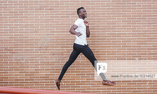Young man wearing white t-shirt jumping at a brick wall