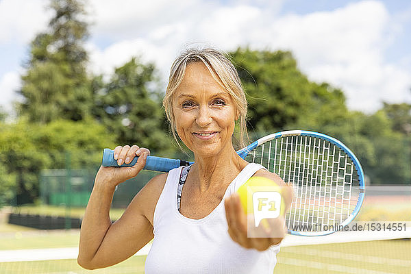 Porträt einer lächelnden reifen Frau  die im Tennisclub einen Tennisball hält