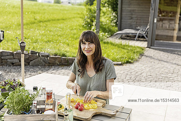 Porträt einer lächelnden Frau die einen Salat auf dem Gartentisch zubereitet