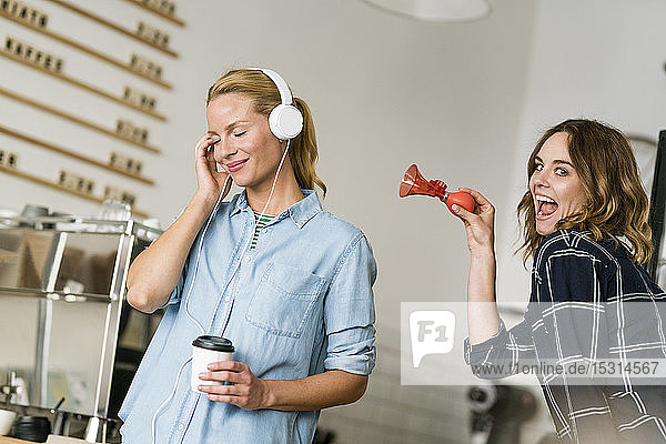 Woman in coffee shop listening music  friend trying to interrupt her with a horn