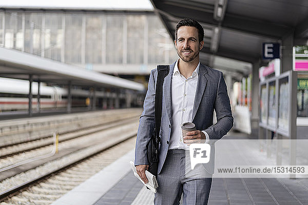 Businessman with takeaway coffee walking on station platform