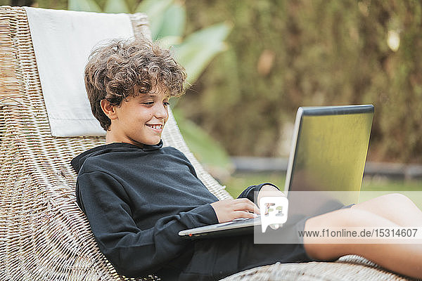Entspannter Junge mit Laptop im Aufenthaltsraum im Garten