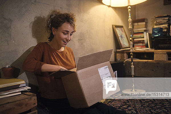 Erstaunte junge Frau packt Paket zu Hause aus