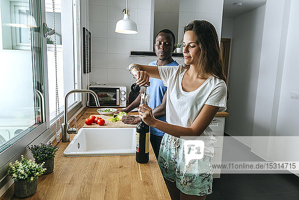 Frau öffnet Weinflasche neben dem Mann in der Küche