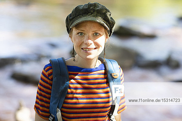 Porträt einer lächelnden Frau mit Rucksack an einem Flussufer
