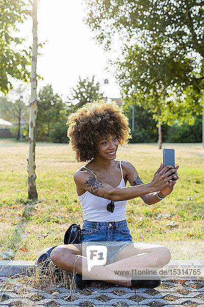 Porträt einer tätowierten jungen Frau die sich im Sommer mit einem Smartphone selbstständig macht