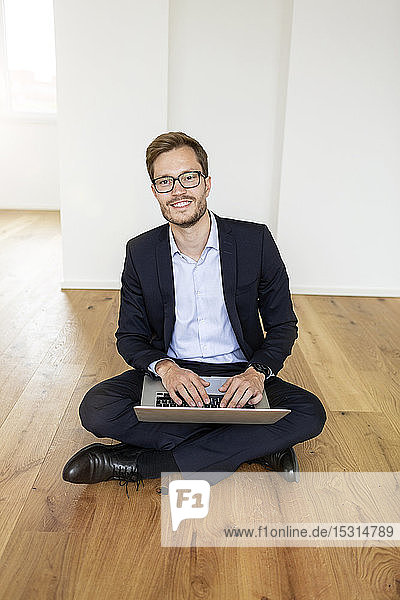 Portrait of a smiling businessman sitting on the floor using laptop