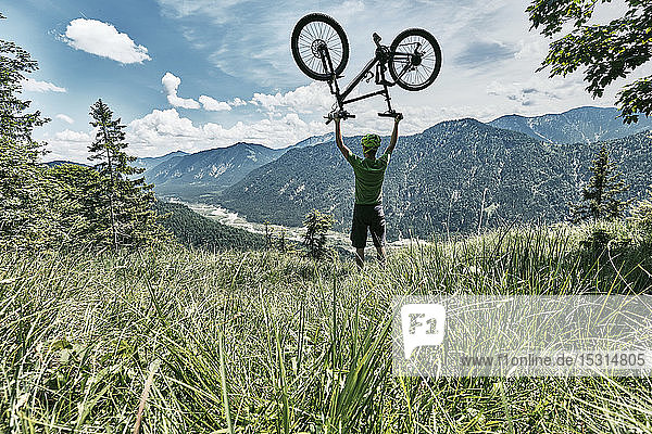 Mountain biker in the mountains holding up his mountain bike  Bavaria  Germany