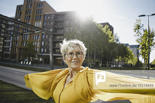 Porträt einer lächelnden reifen Frau im Gegenlicht mit gelber Kleidung