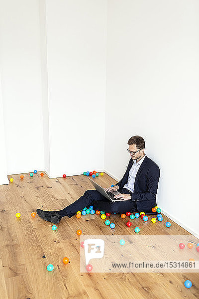 Businessman sitting on the floor using laptop surrounded by colourful balls