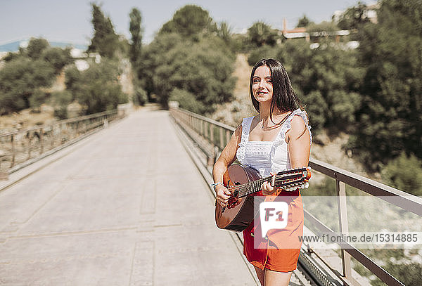 Young woman playing guitar  standing on bridge