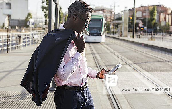 Young businessmann using his smartphone and waiting for the tram