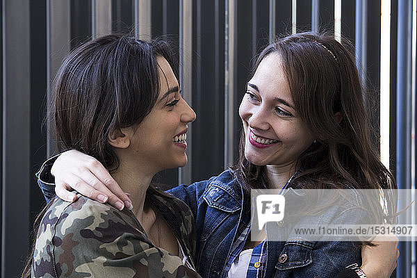 Lächelnde junge Frau mit ihrer besten Freundin an einer Wand