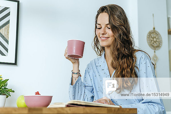 Lächelnde junge Frau liest während des Frühstücks zu Hause