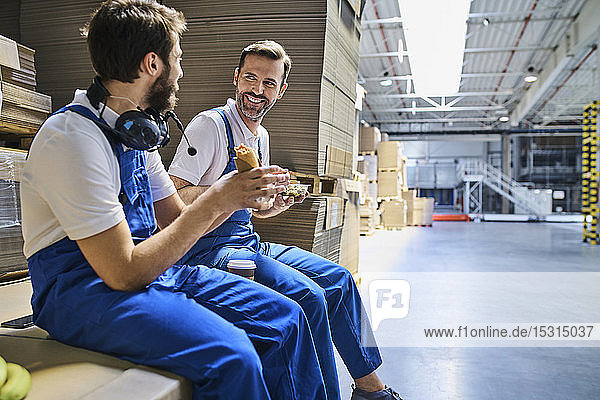 Zwei glückliche Arbeiter machen Mittagspause in der Fabrik