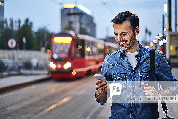 Mann benutzt Smartphone  während er abends auf die öffentliche Straßenbahn wartet