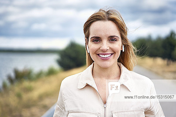 Porträt einer lächelnden Frau mit drahtlosen Kopfhörern in der Natur
