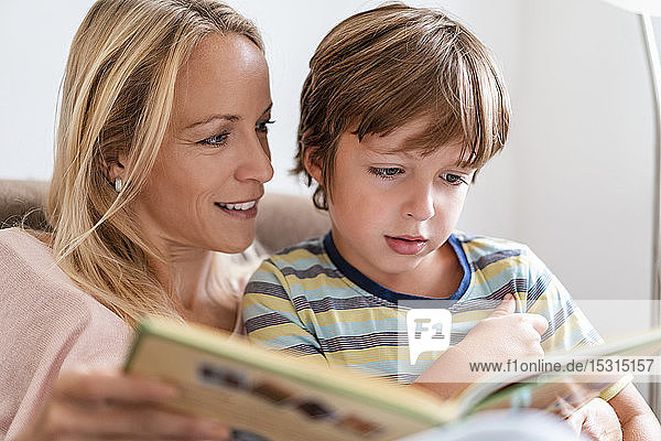 Mutter und Sohn lesen zu Hause auf der Couch gemeinsam ein Buch