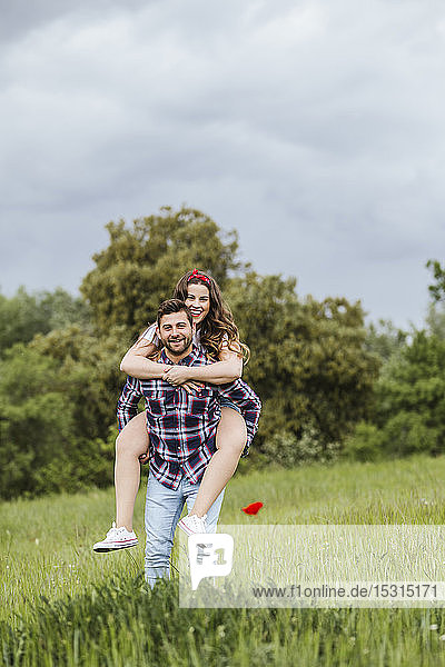 Young man carrying girlfriend piggyback in nature