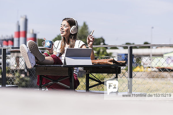 Junge Frau entspannt sich in einem Biergarten mit Kopfhörer und Tablette