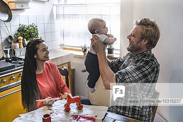 Family lifting up baby at kitchen table at home