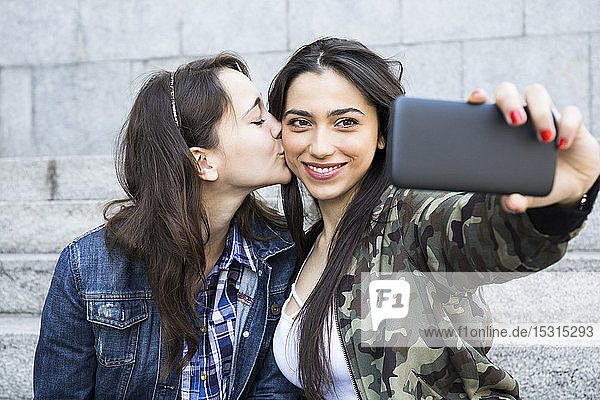 Frau küsst ihren Freund auf die Wange  während sie Selfie nimmt