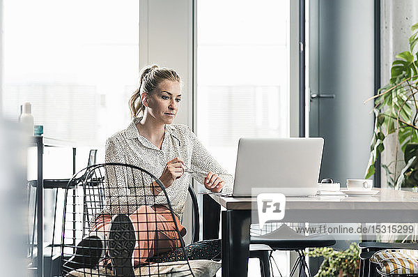Geschäftsfrau  die im Büro am Tisch sitzt und einen Laptop benutzt