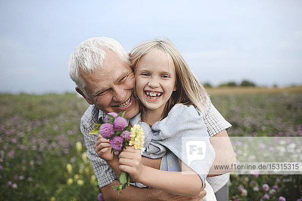 Porträt von lachendem Grossvater und Enkelin mit gepflückten Blumen auf einer Wiese