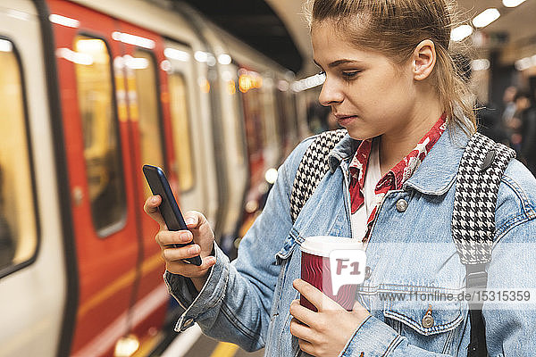 Junge Frau an der U-Bahn-Station mit einem Smartphone