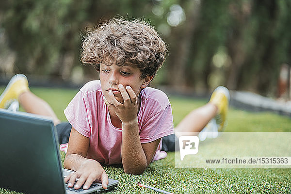 Junge liegt mit Laptop im Gras