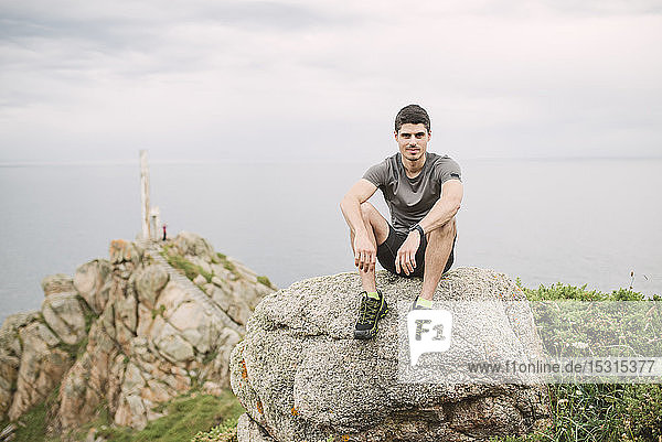 Porträt eines Trailrunners der auf einem Felsen in der Küstenlandschaft sitzt Ferrol Spanien
