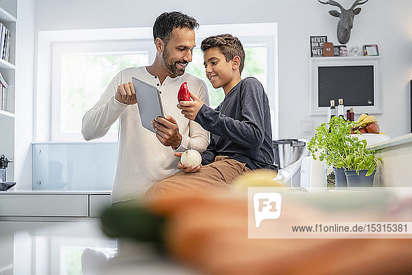 Vater und Sohn verwenden Tabletten und kochen gemeinsam in der Küche zu Hause