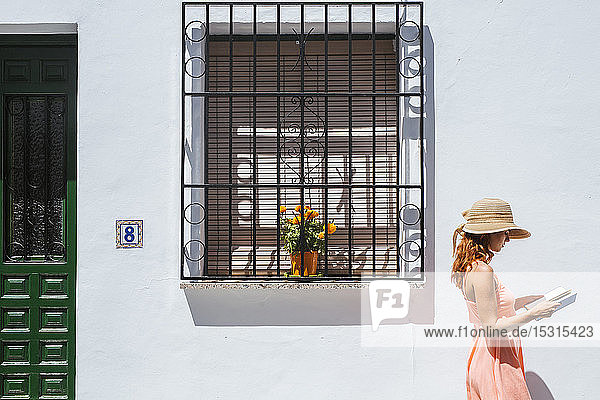 Redheaded young woman reading a book in front of a house Frigiliana Malaga Spain