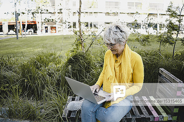 Reife Frau sitzt auf Bank im Freien und benutzt Laptop