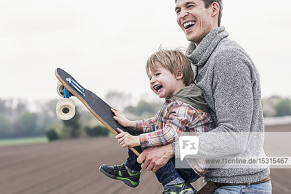Vater und Sohn amüsieren sich  spielen mit dem Skateboard im Freien
