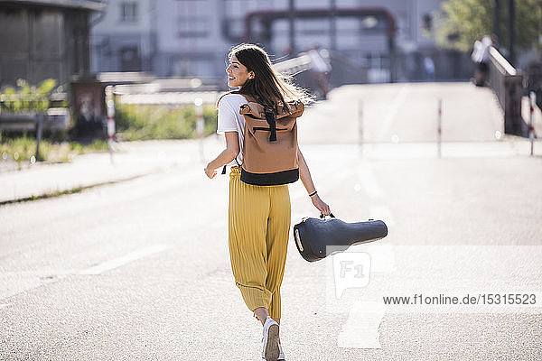 Glückliche junge Frau mit Geigenkoffer auf der Strasse