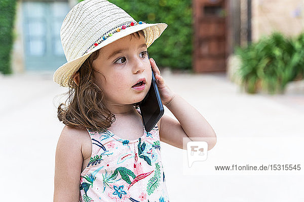 Portrait of toddler girl with straw hat on the phone