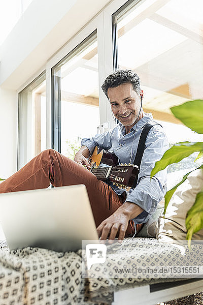 Mature man practising on the guitar using laptop and earphones