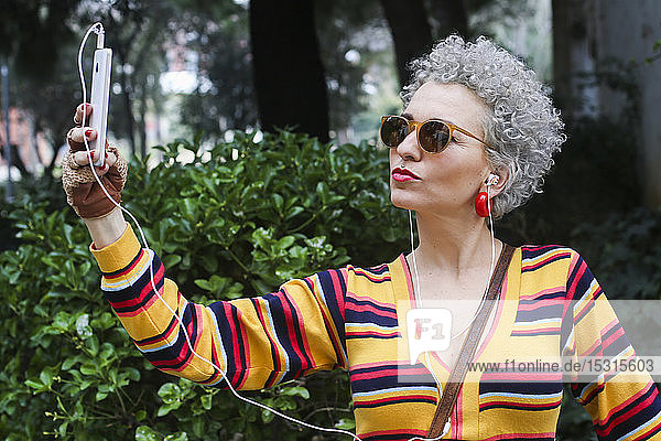 Porträt einer gepiercten reifen Frau  die sich mit einem Smartphone im Freien selbstständig macht