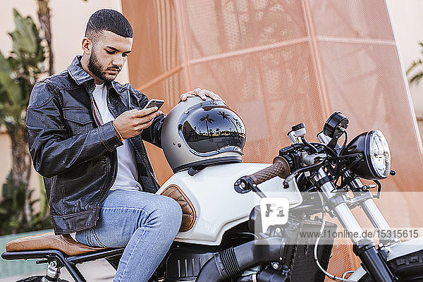 Junger Mann sitzt auf seinem Motorrad und benutzt sein Handy
