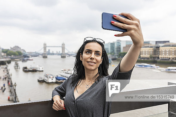 Frau  die sich in der Stadt mit der Tower Bridge im Hintergrund ein Selfie gönnt  London  UK