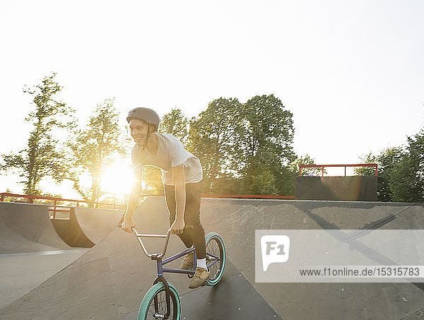 Glücklicher junger Mann fährt BMX-Rad im Skatepark bei Sonnenuntergang