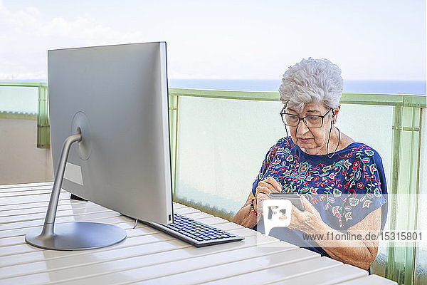 Ältere Frau mit Smartphone auf der Terrasse