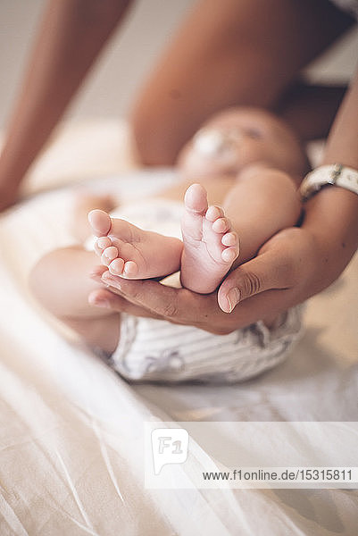 Die Hand der Mutter hält winzige Füße des kleinen Jungen  Nahaufnahme