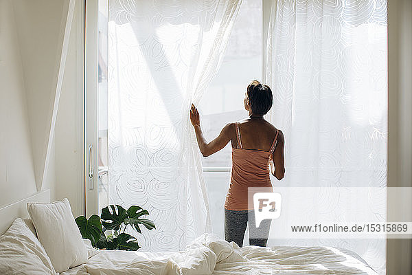 Frau  die zu Hause am Fenster im Schlafzimmer steht
