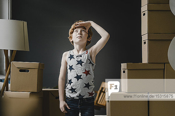 Porträt eines rothaarigen Jungen  der neben Pappkartons steht und nach oben schaut