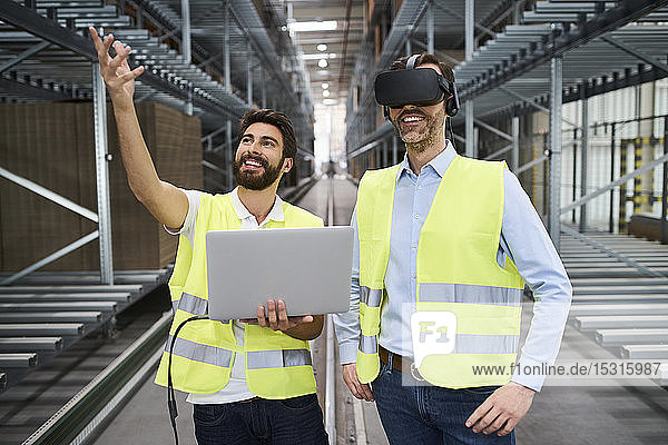 Mann mit Laptop und Geschäftsmann mit VR-Brille in der Fabrik